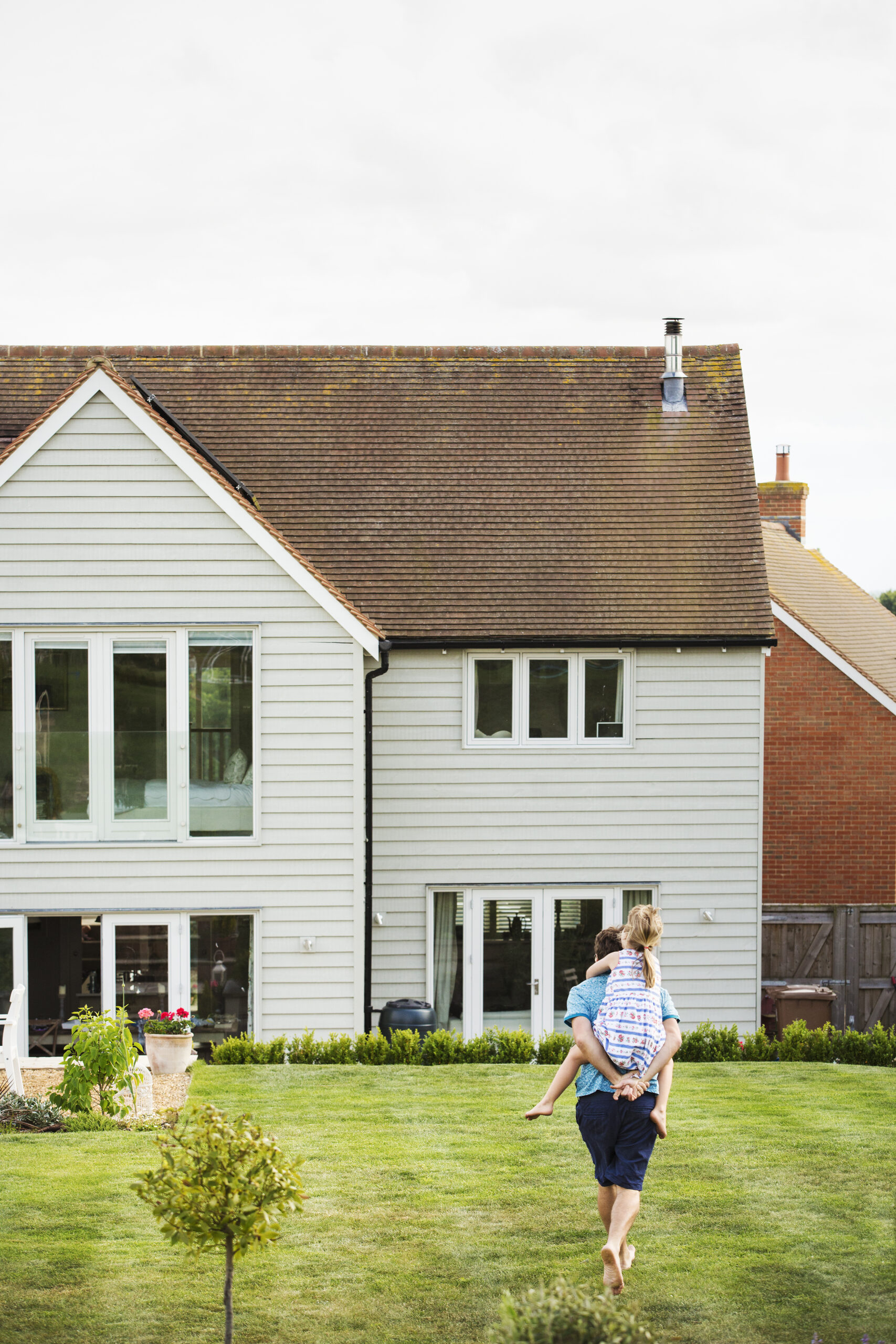 Rear view of a man walking across a lawn, giving a piggyback to daughter. Minority Family Qualifies for HomeBoost Down Payment Assistance